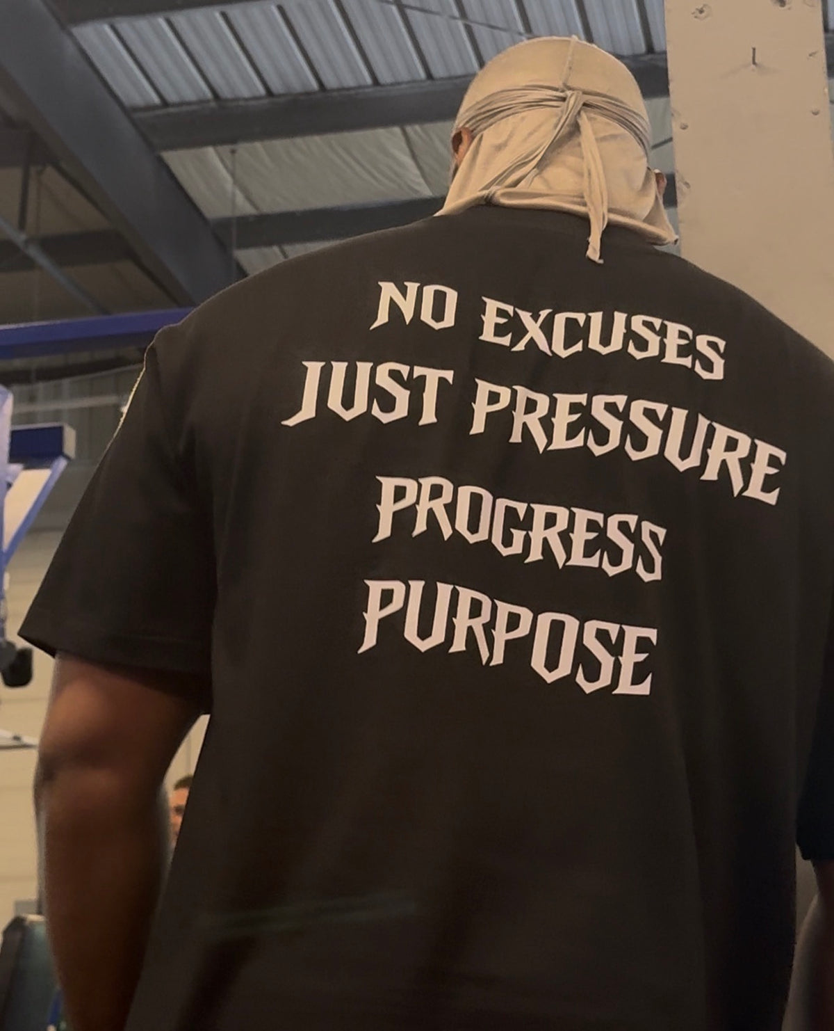 Close-up of Strap-Up Fitness Pressure Tee No Excuses Just Pressure Progress Purpose back print in the gym